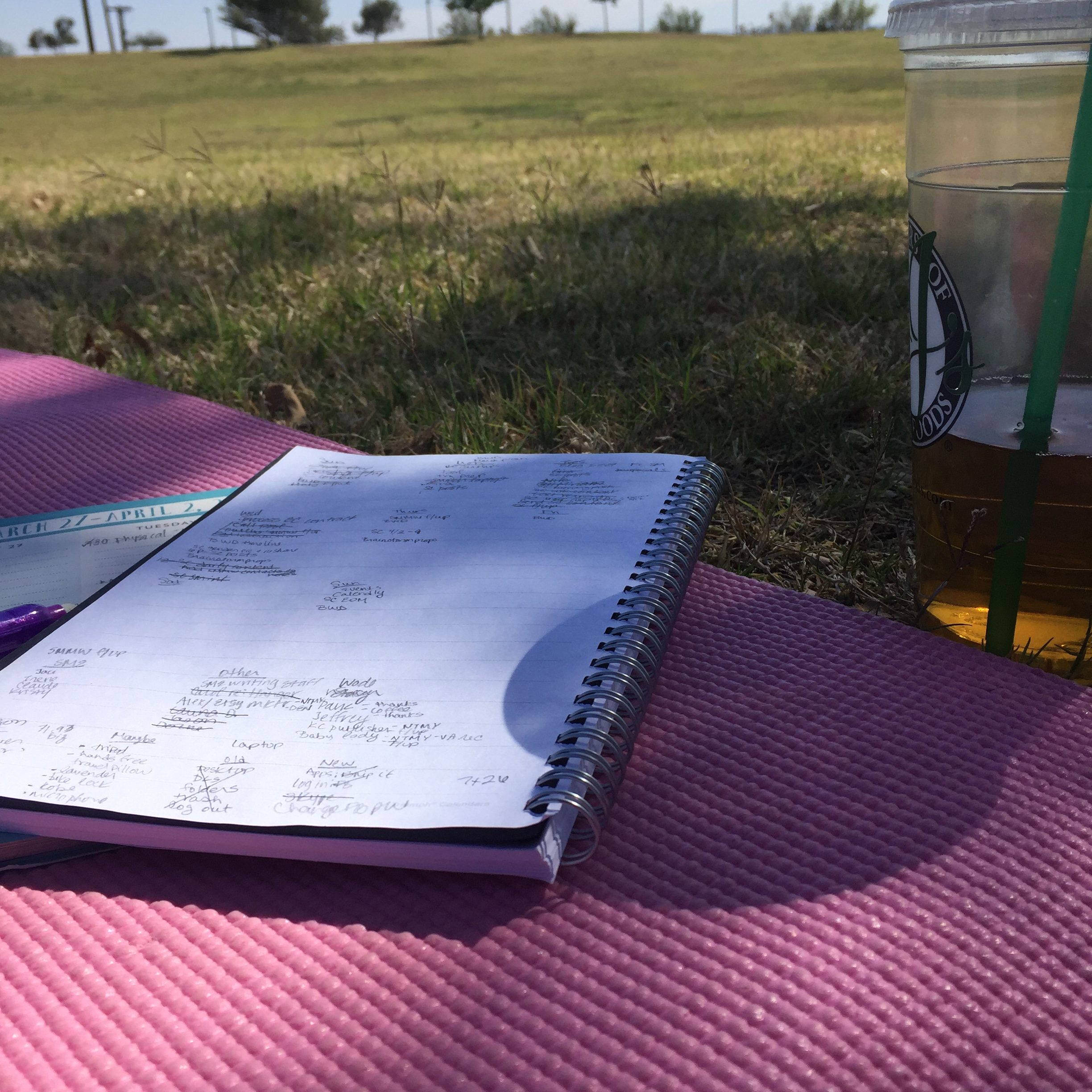 Working outdoors on a yoga mat with iced tea. Notebook and pen in hand. 